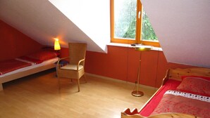 Une petite pièce chaleureuse avec un plafond en pente, un simple lit en bois, une chaise et une lampe sur pied.