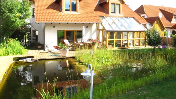 Une maison avec un grand étang, une terrasse en bois et un jardin.