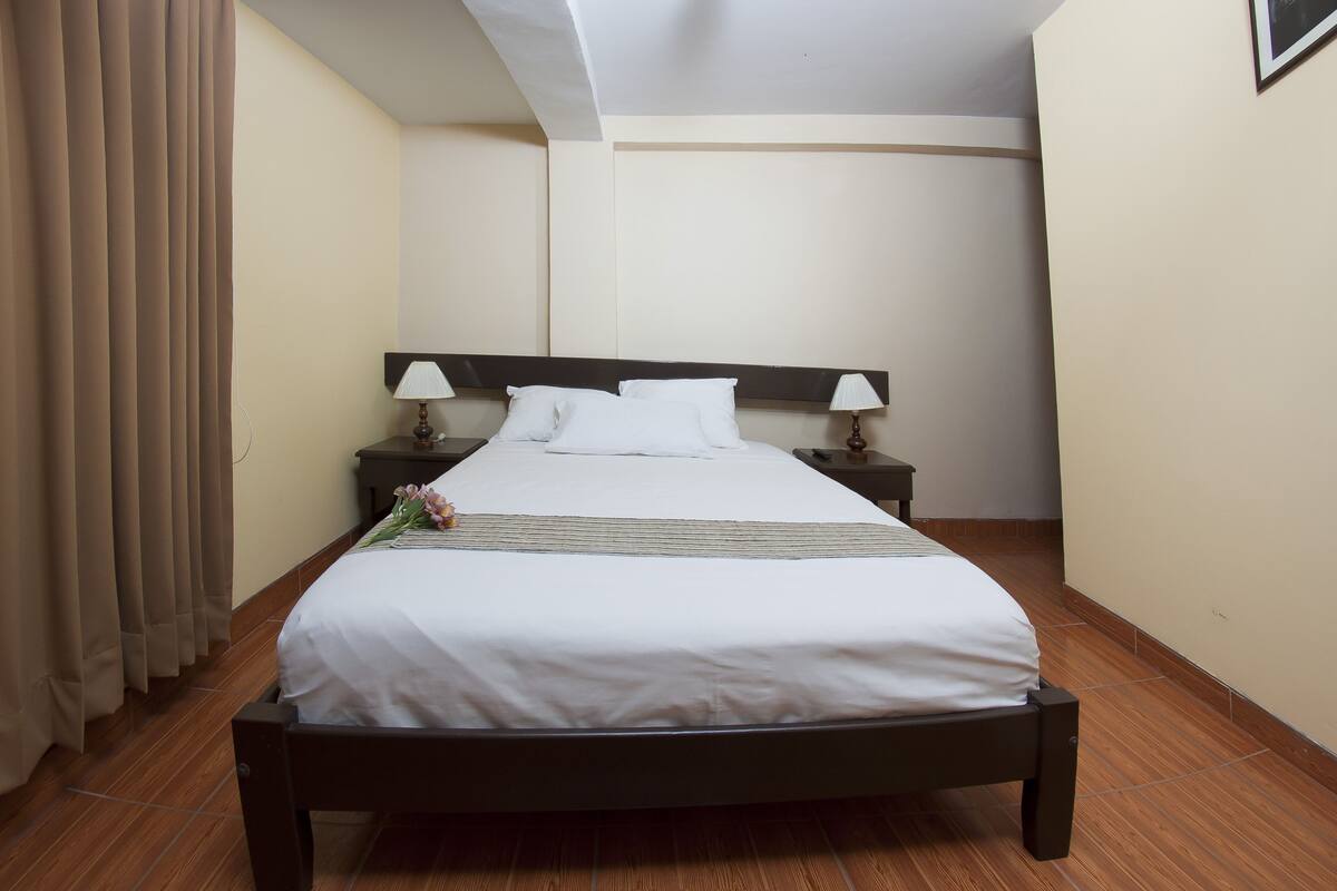 Ein ordentlich gemachtes Bett mit weißen Leinen, zwei Nachttische mit Lampen und ein Holzboden.