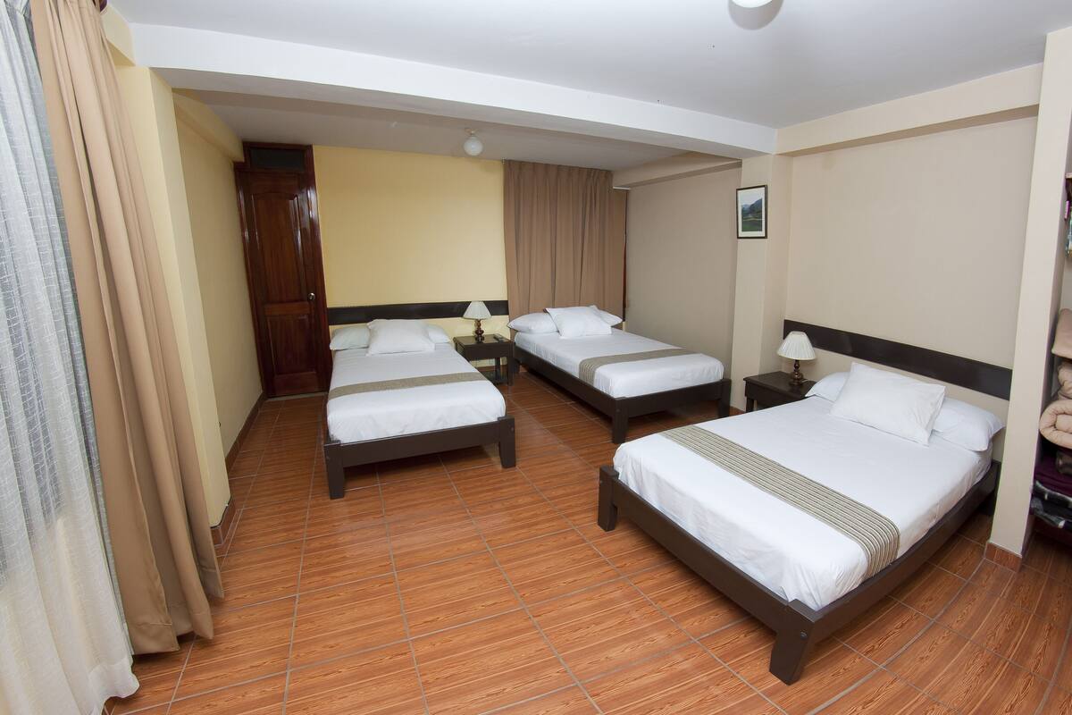 Ein Hotelzimmer mit drei Betten, Holzboden und beigen Wänden.