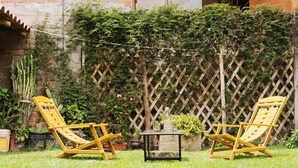 A garden with two wooden lounge chairs and a small table, surrounded by a brick wall and a wooden lattice fence. - Yucay Plaza Inn (Yucay)