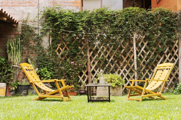 Relax in a serene outdoor space with two lounge chairs and a small table, surrounded by lush greenery.