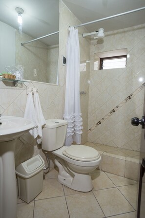 Features a sink, toilet, shower, and mirror, with a window above the toilet and a tiled floor.
