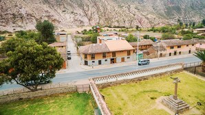 A rural village with traditional buildings, a paved road, and a grassy area with a cross monument. - Yucay Plaza Inn (Yucay)