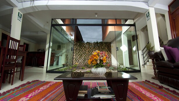 A modern living room with a glass partition, a coffee table with books, and a colorful rug. - Yucay Plaza Inn (Yucay)