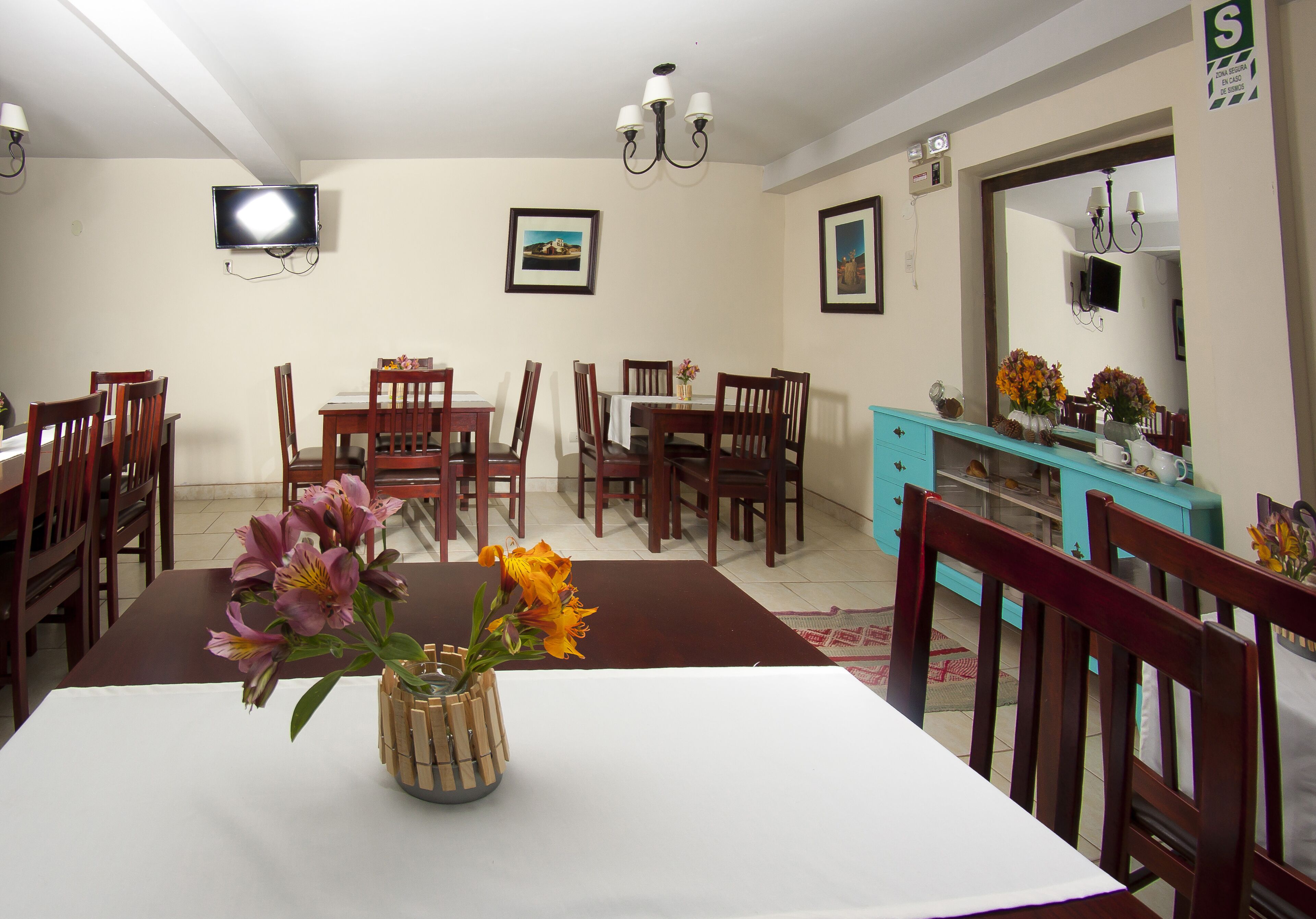 Un comedor con una mesa preparada para cuatro personas, rodeada de sillas de madera, un armario azul y un televisor montado en la pared.