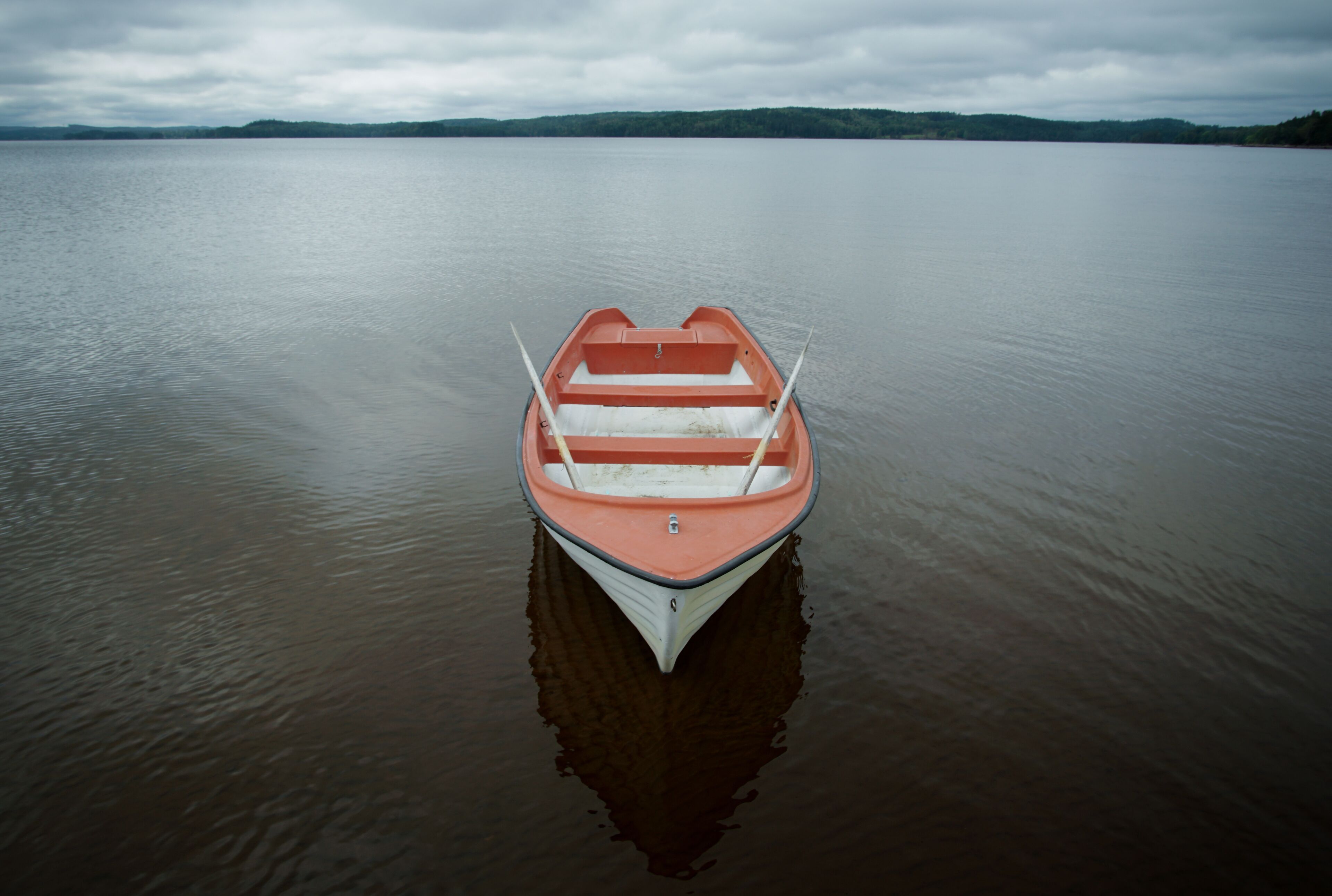 Un petit bateau orange à l’intérieur blanc, flottant sur une eau calme.