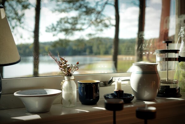 A table with a bowl, a vase with dried flowers, a mug, a candle, and a glass container.