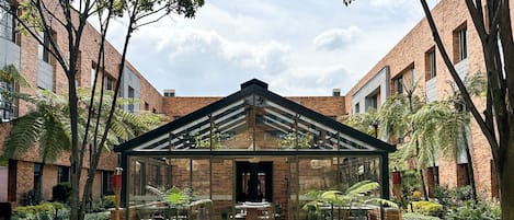 A courtyard with a glass-roofed pavilion, brick buildings, and green lawns.