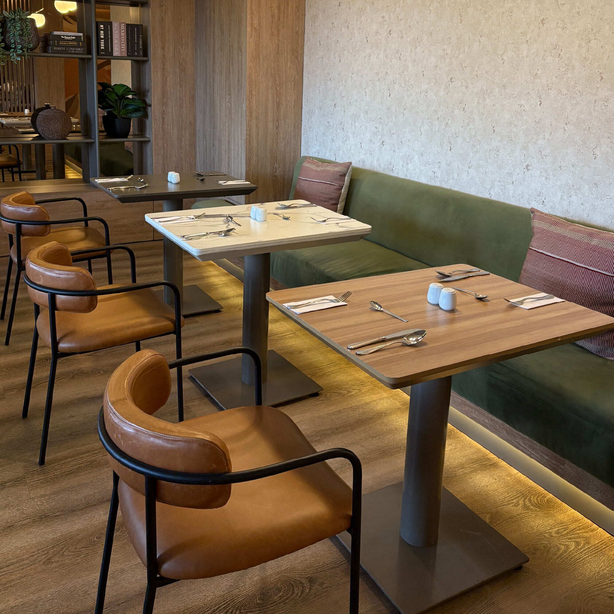 A restaurant interior with wooden tables, leather chairs, and a green sofa.
