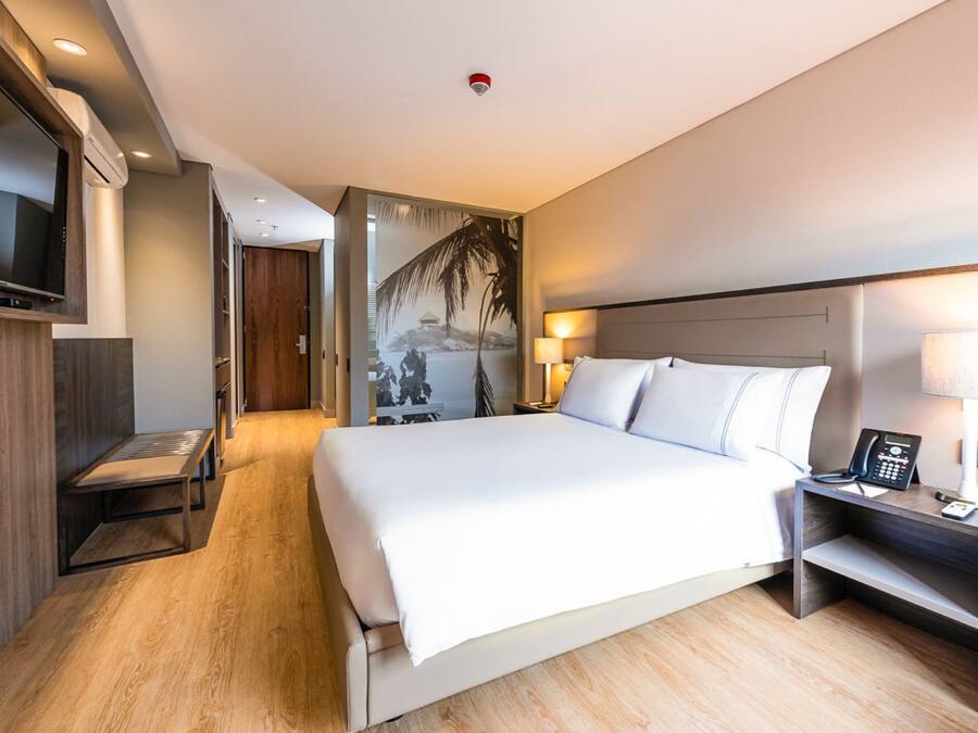 A modern hotel room with a large bed, bedside tables, a TV, and a painting on the wall.