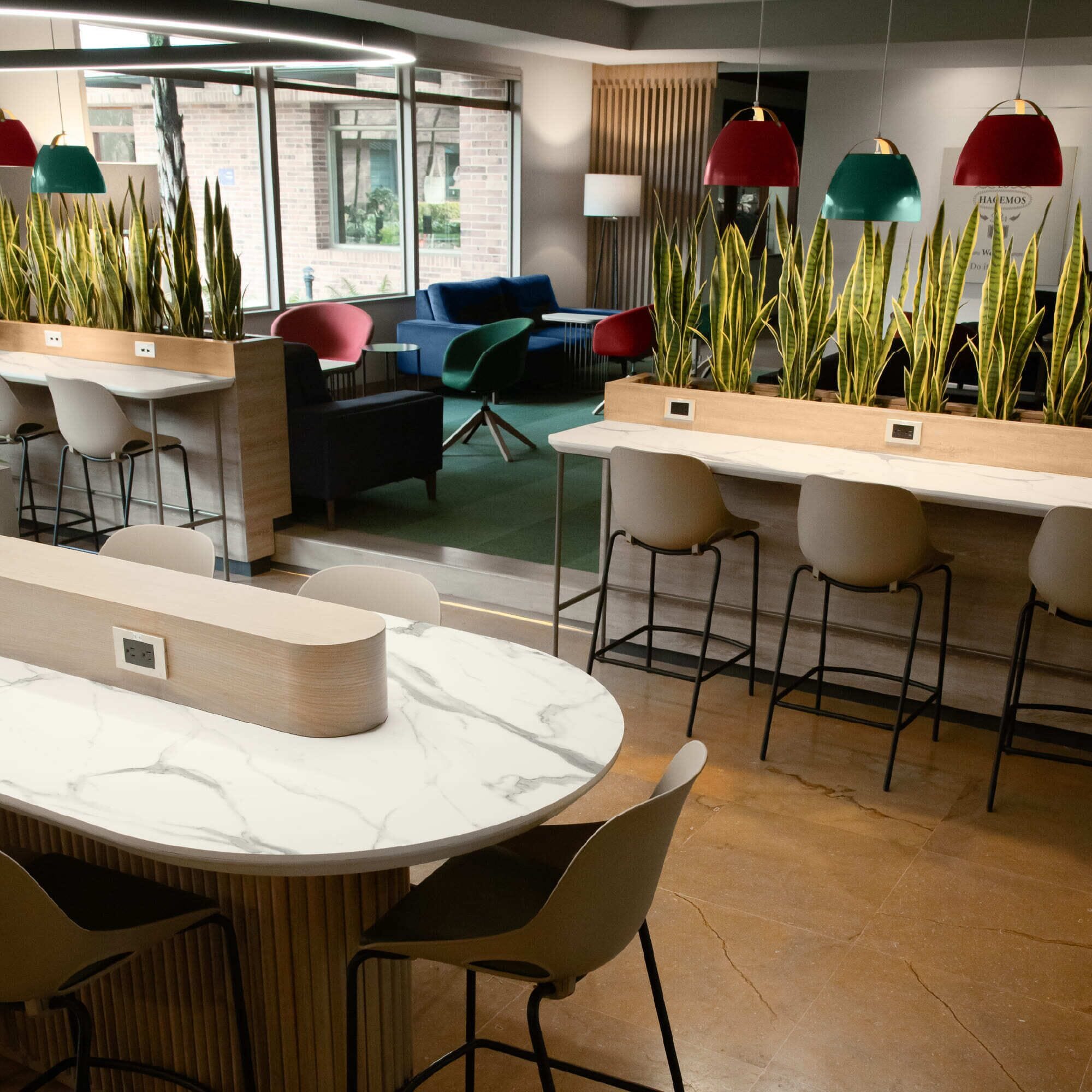 A modern office space with a round marble table, bar stools, and potted plants.