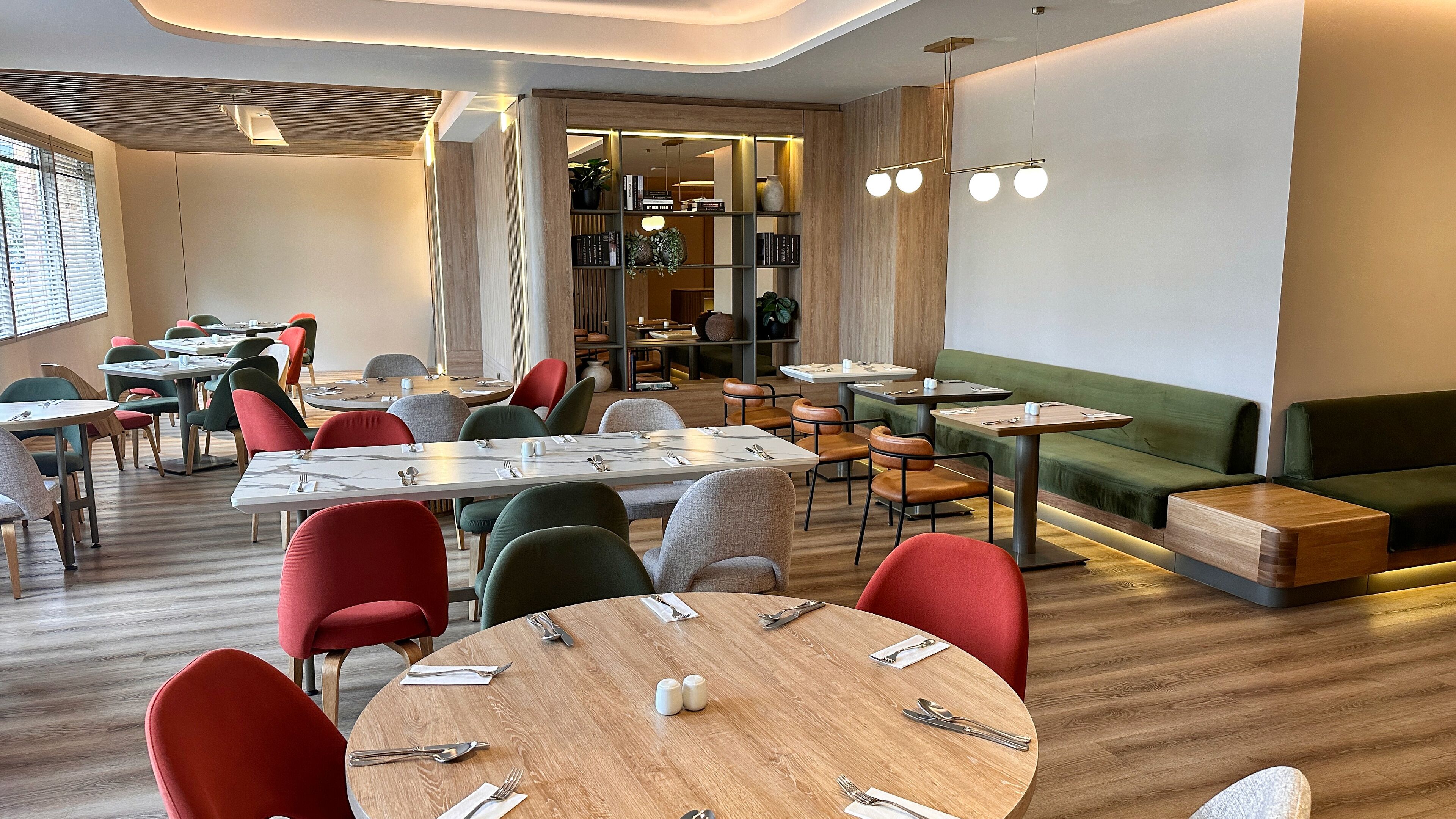 Un restaurante moderno con mesas redondas, sillas rojas y verdes, y un sofá verde.