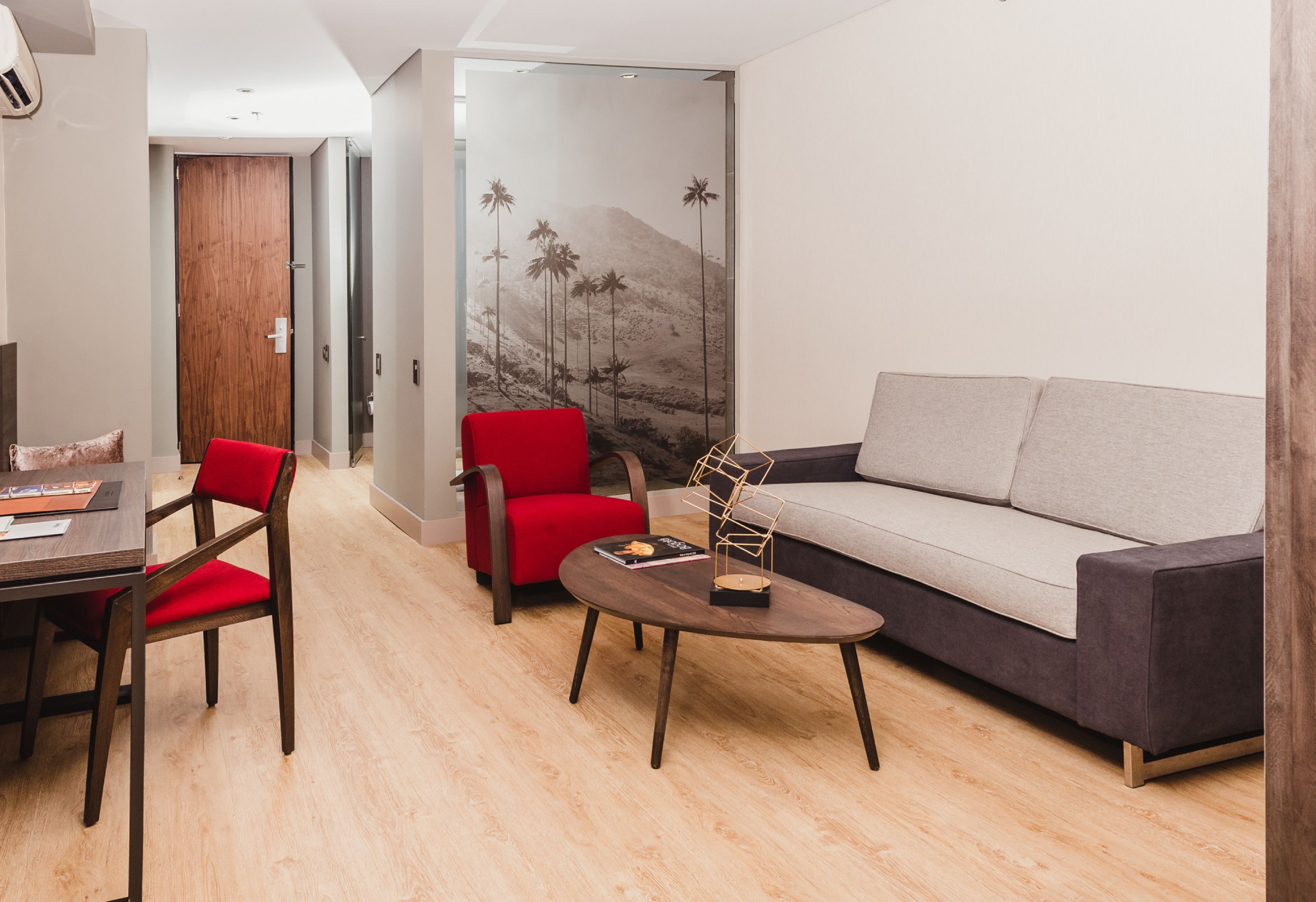 A modern living room with a sofa, two red chairs, a coffee table, and a wooden floor.