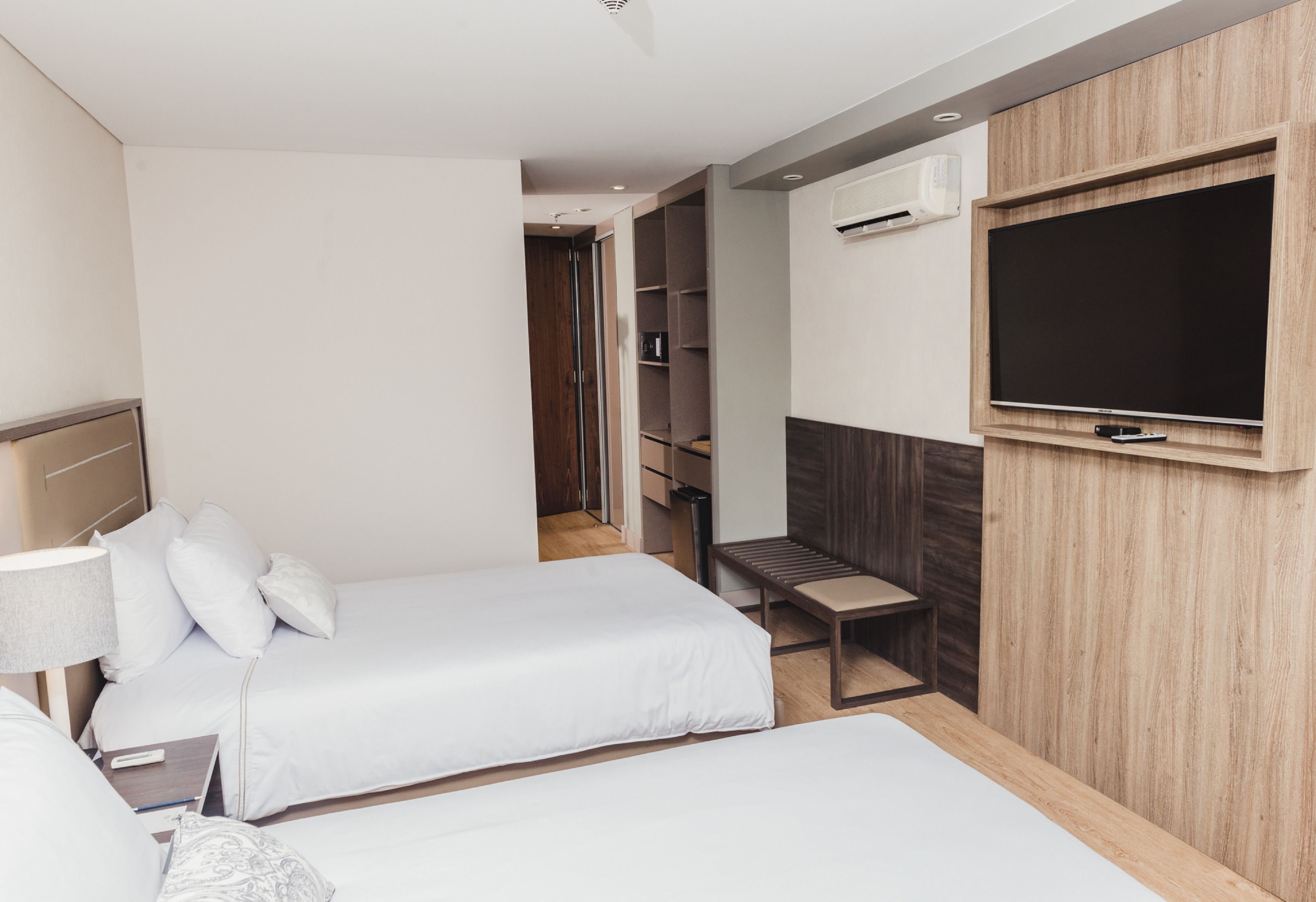 A hotel room with two beds, a TV, a wardrobe, and a bench.
