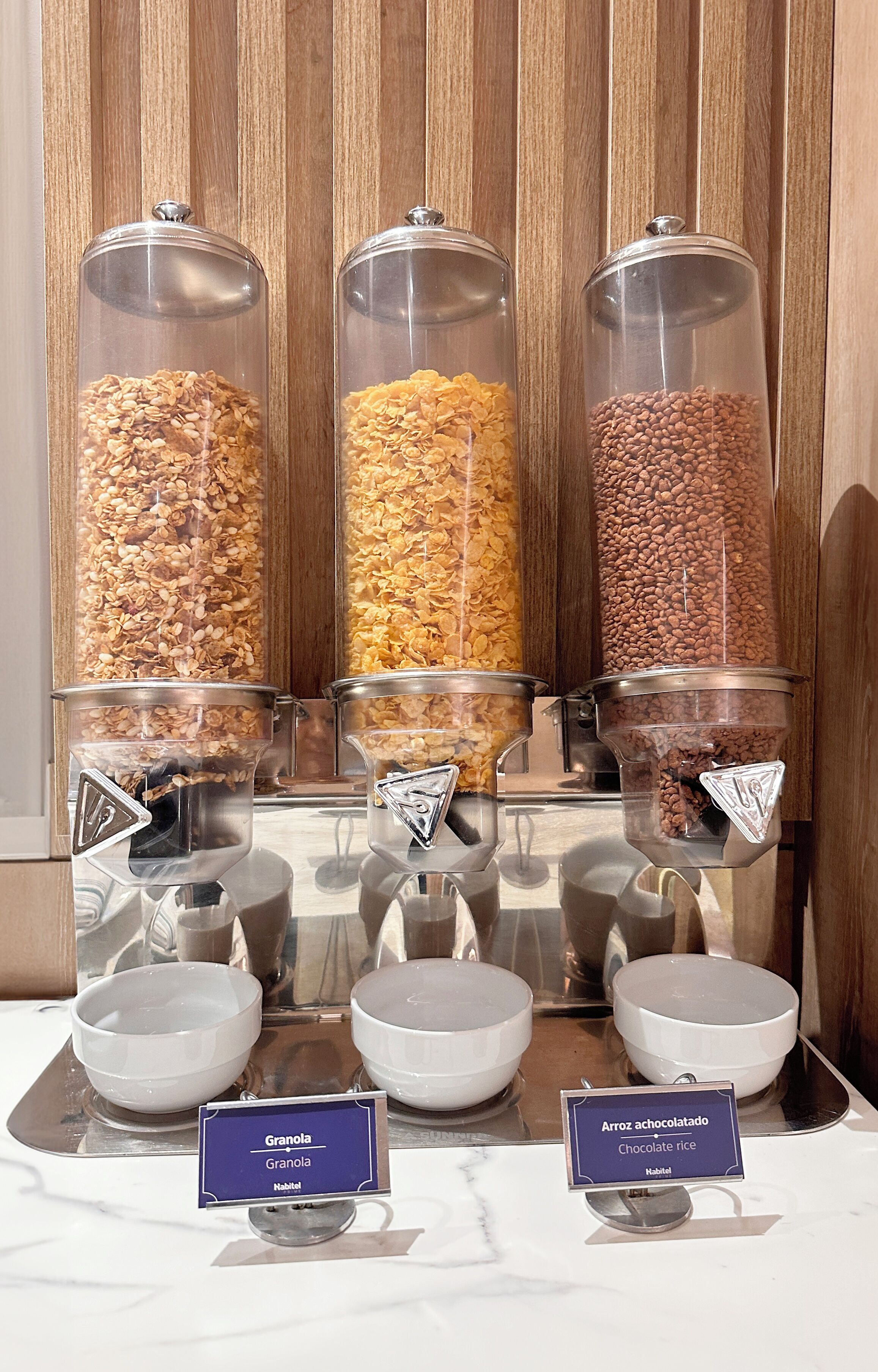 A breakfast buffet with labeled containers of granola and chocolate rice.