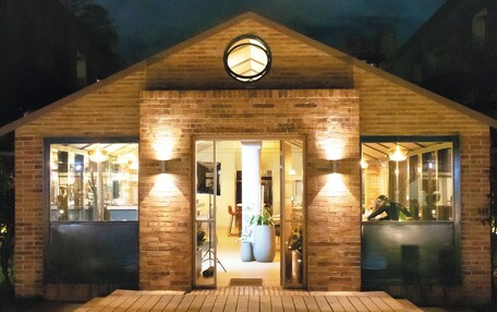 A wooden building with a brick facade, a central door, and two illuminated windows.