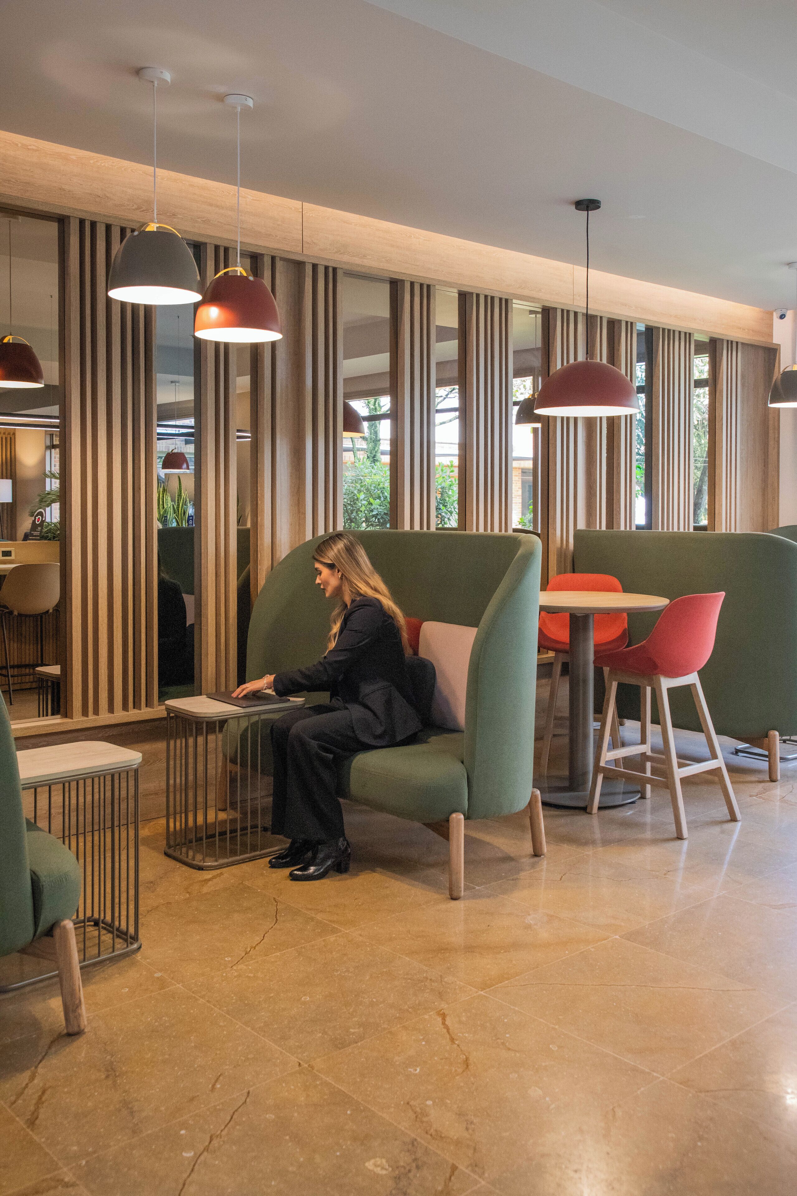 A modern interior with seating areas, a person using a laptop, and vertical wooden panels.