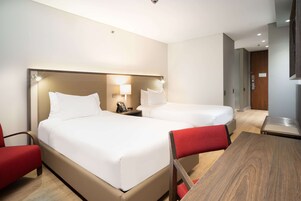 Hotellihuone, jossa on kaksi sänkyä, työpöytä ja tuoli.