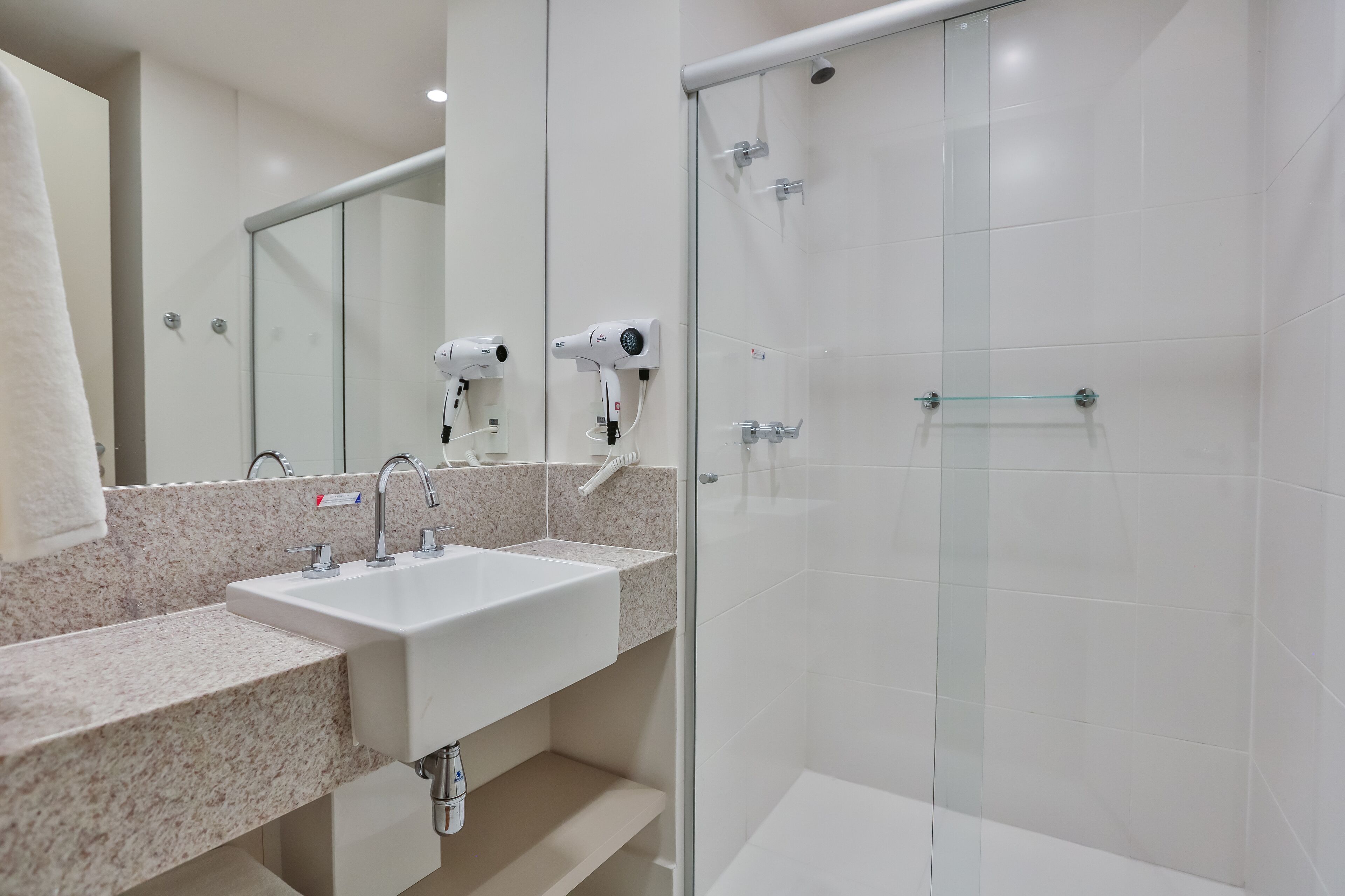 A modern bathroom with a granite countertop sink, a glass shower enclosure, and a hairdryer mounted on the wall.