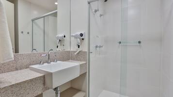 A modern bathroom with a granite countertop sink, a glass shower enclosure, and a hairdryer mounted on the wall.