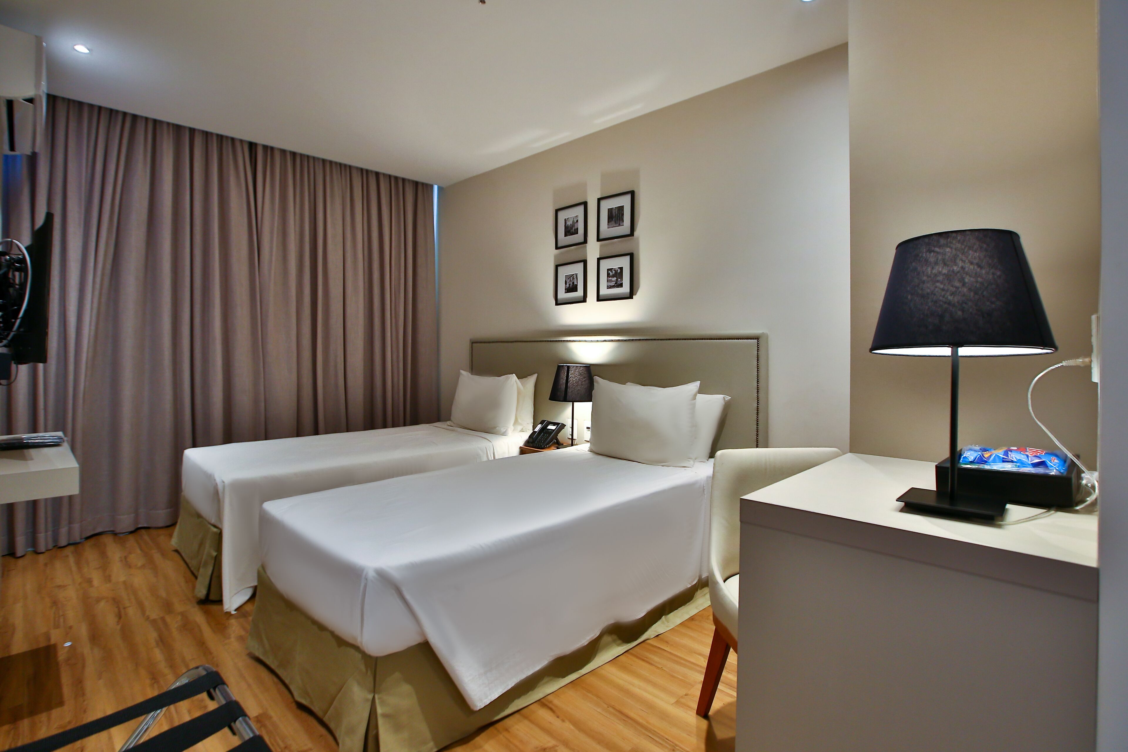 A hotel room with two single beds, a desk with a lamp, a chair, a TV, and a curtain.