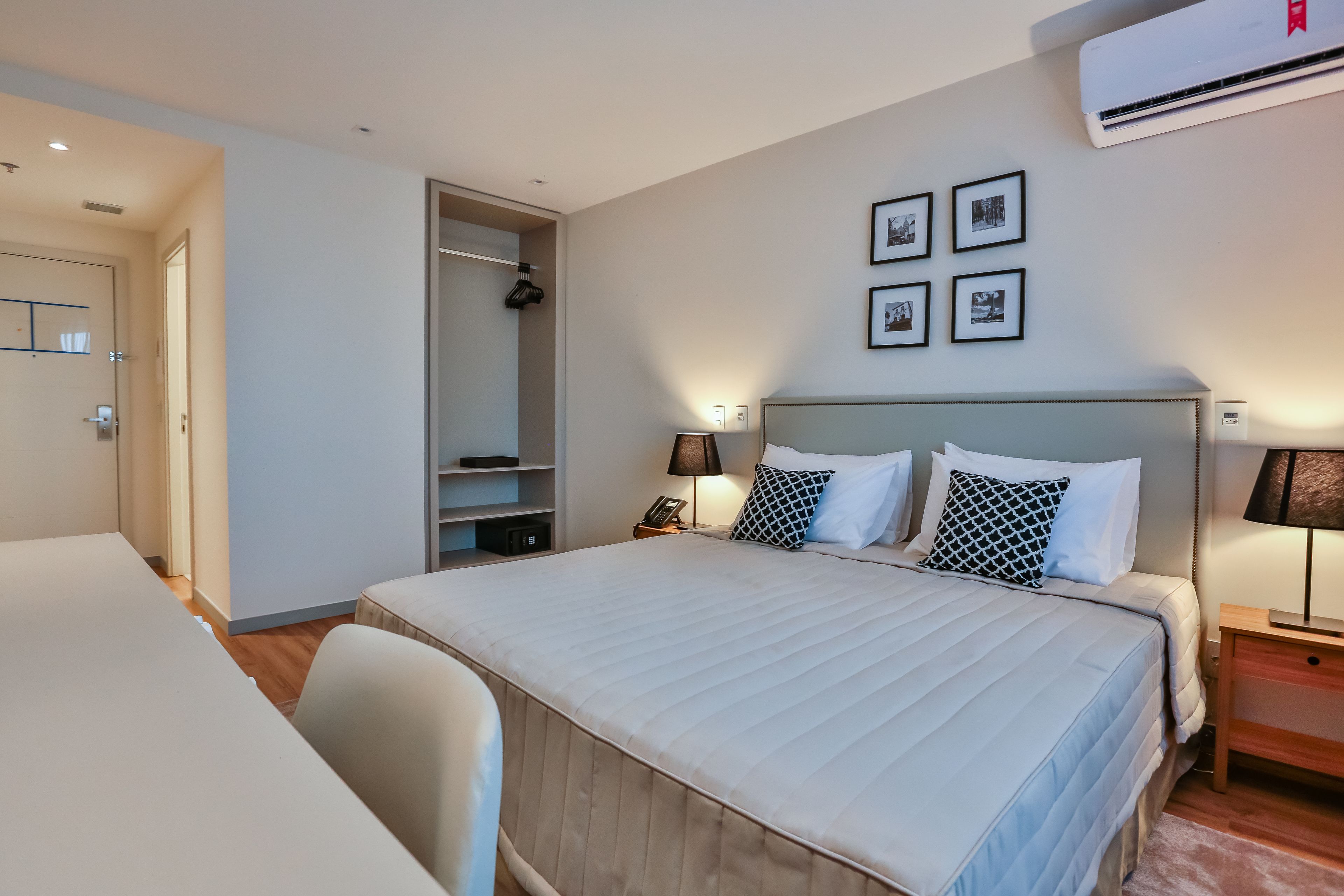 Una habitación de hotel ordenada con una cama grande, mesitas de noche, un escritorio y un armario.