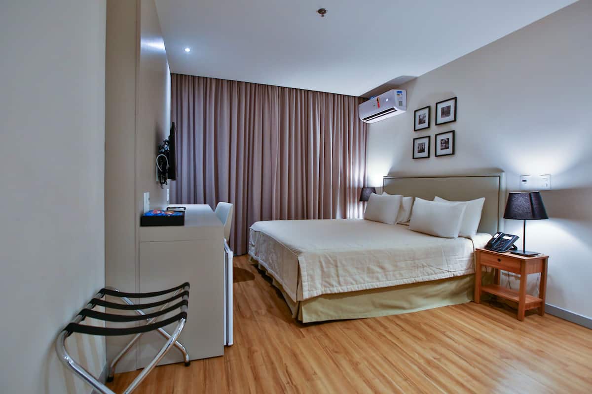 Una habitación de hotel con cama, mesita de noche, silla y aire acondicionado.