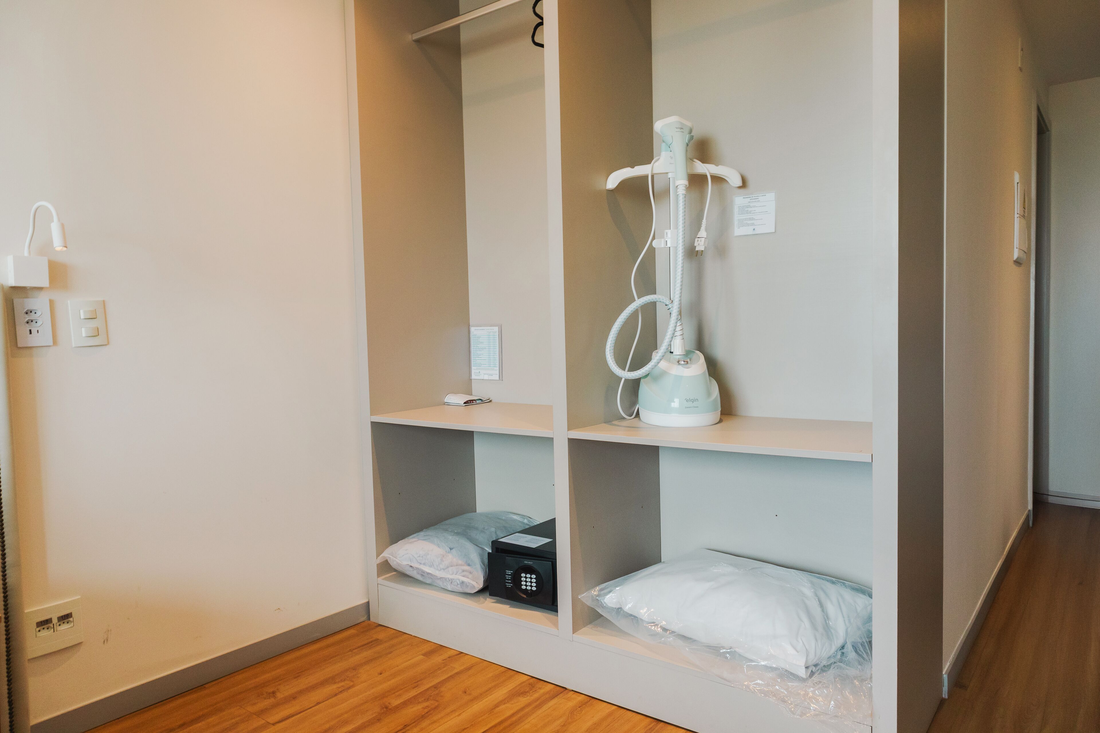 Ein Hotelzimmer mit integrierter Minibar, einem weißen Nachttisch, einer Steckdose und einem an der Wand montierten Heizgerät.
