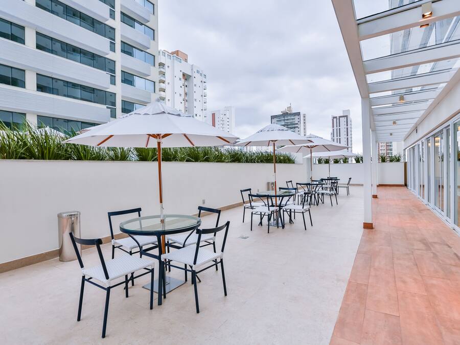 Een dakterras met buitenmeubilair, glazen balustrades en uitzicht op omliggende gebouwen.