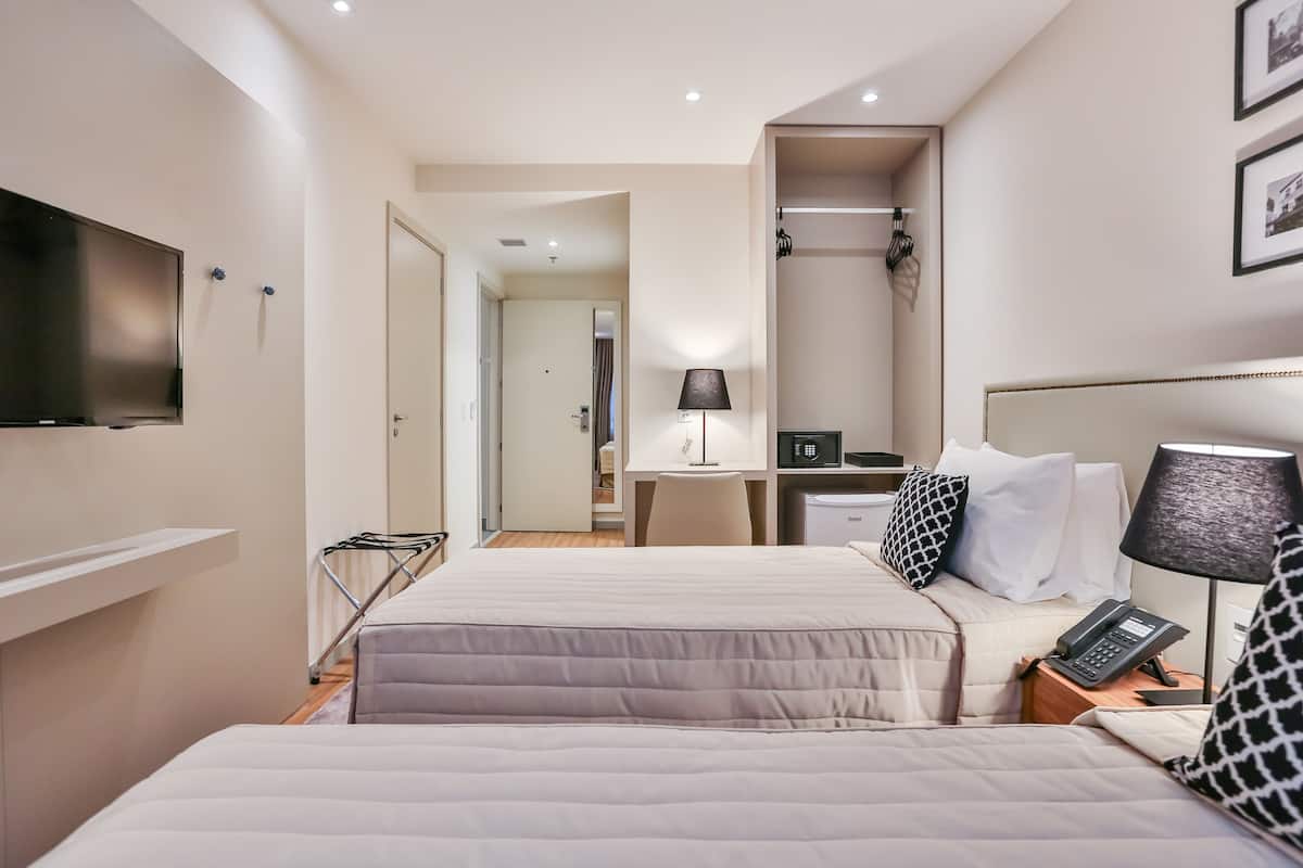 Habitación de hotel con dos camas, un escritorio con computadora, teléfono y televisor montado en la pared.