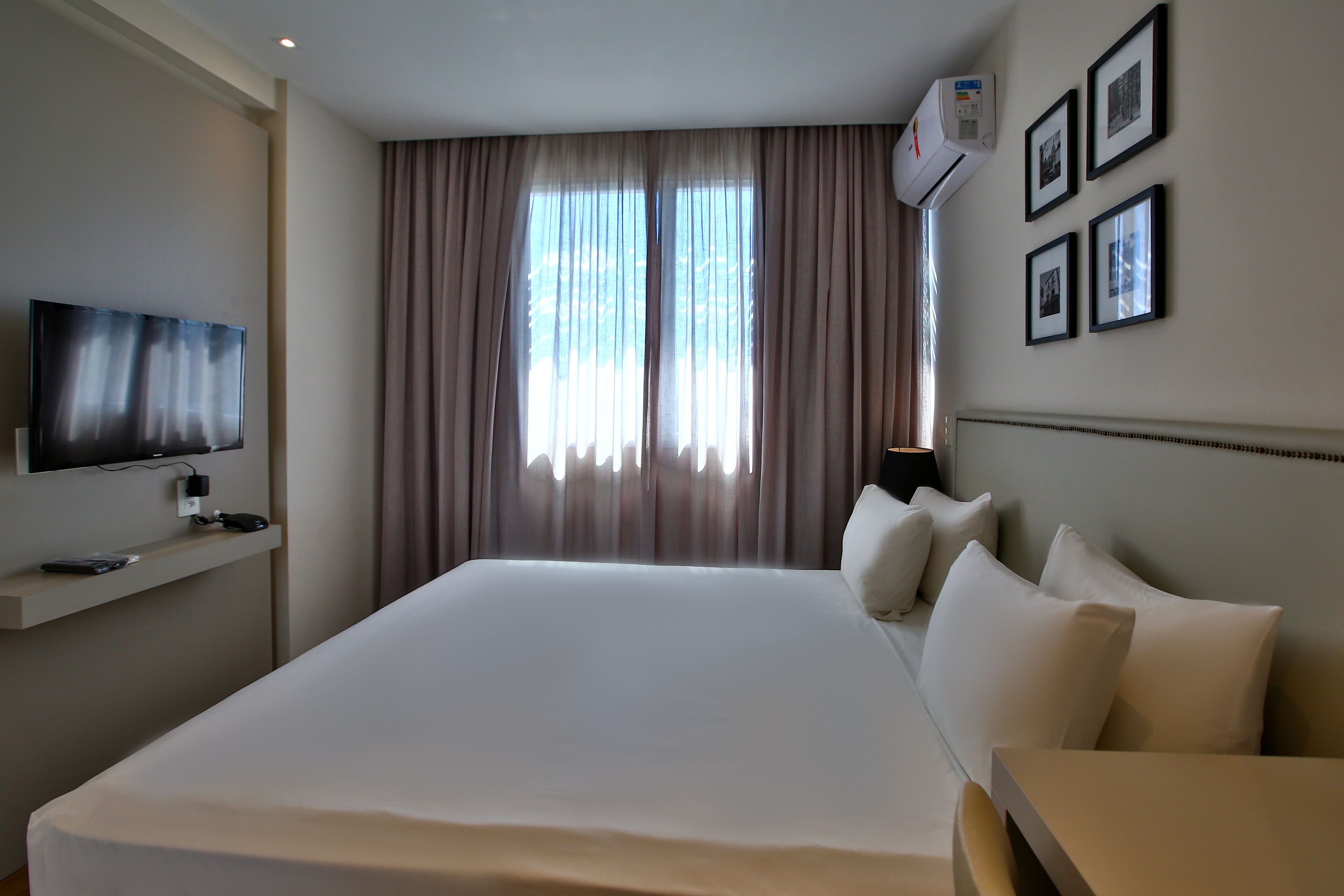 A hotel room with a large bed, a flat-screen TV mounted on the wall, and a window with curtains.