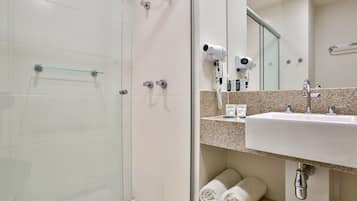 A modern bathroom with a glass shower enclosure, a sink with a mirror above it, and neatly rolled towels on a shelf.