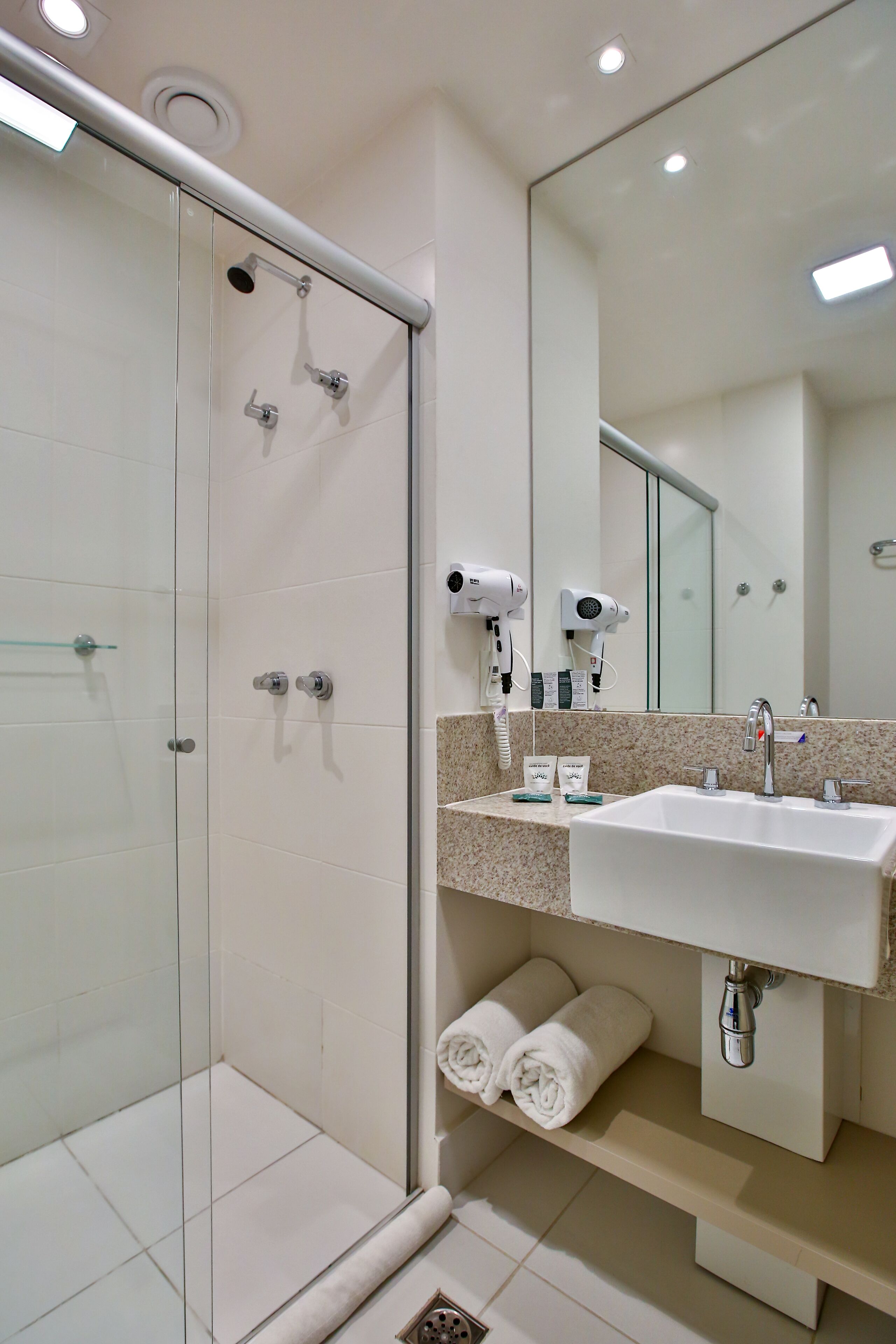 A modern bathroom with a glass shower enclosure, a sink with a mirror, and a towel rack.