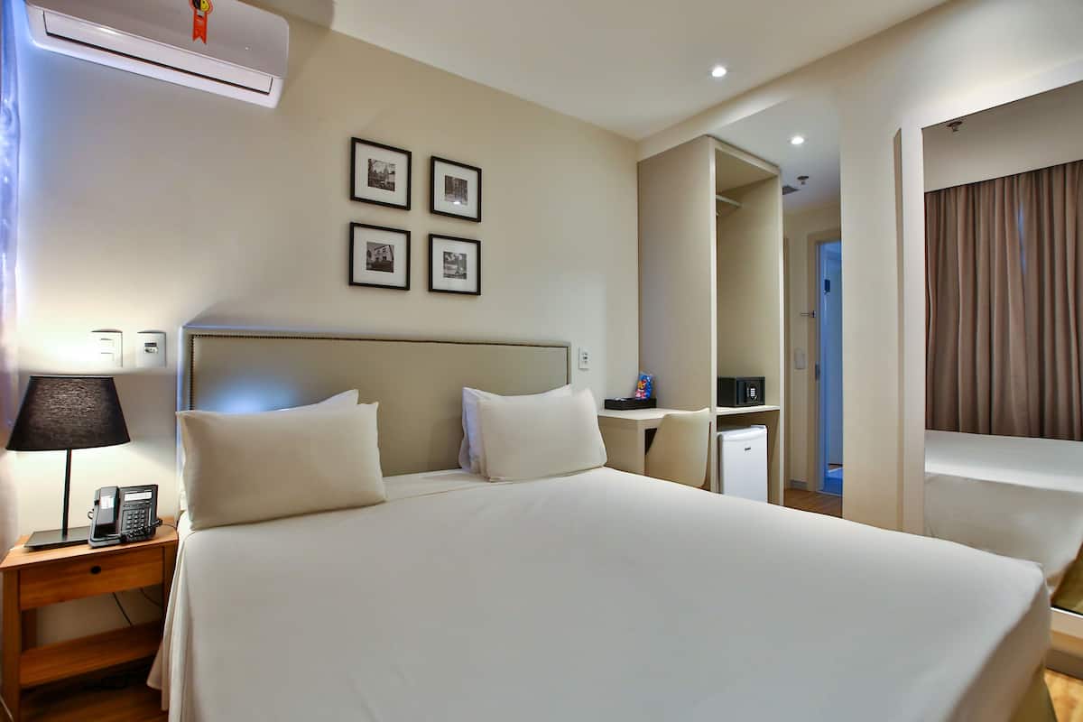 Habitación de hotel con una cama grande, mesita de noche, lámpara, teléfono y aire acondicionado.