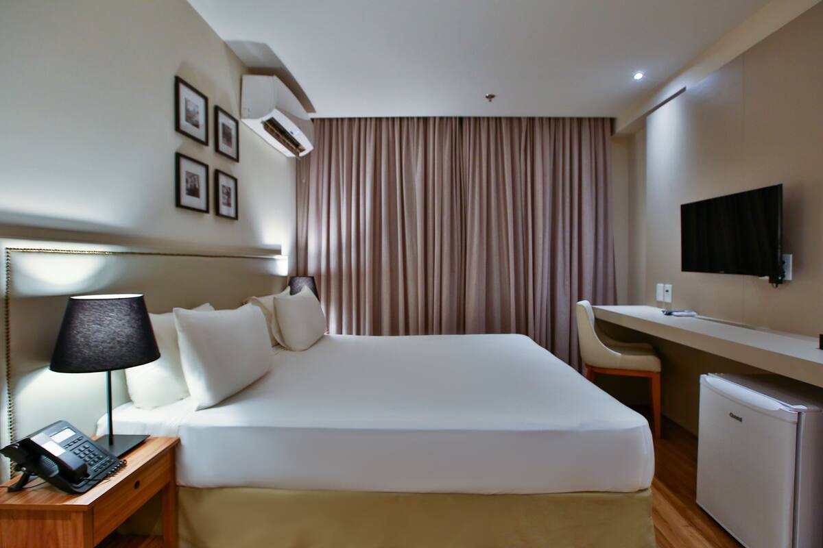 Habitación de hotel con cama, lámpara de noche, escritorio, silla, televisor y un mini refrigerador.
