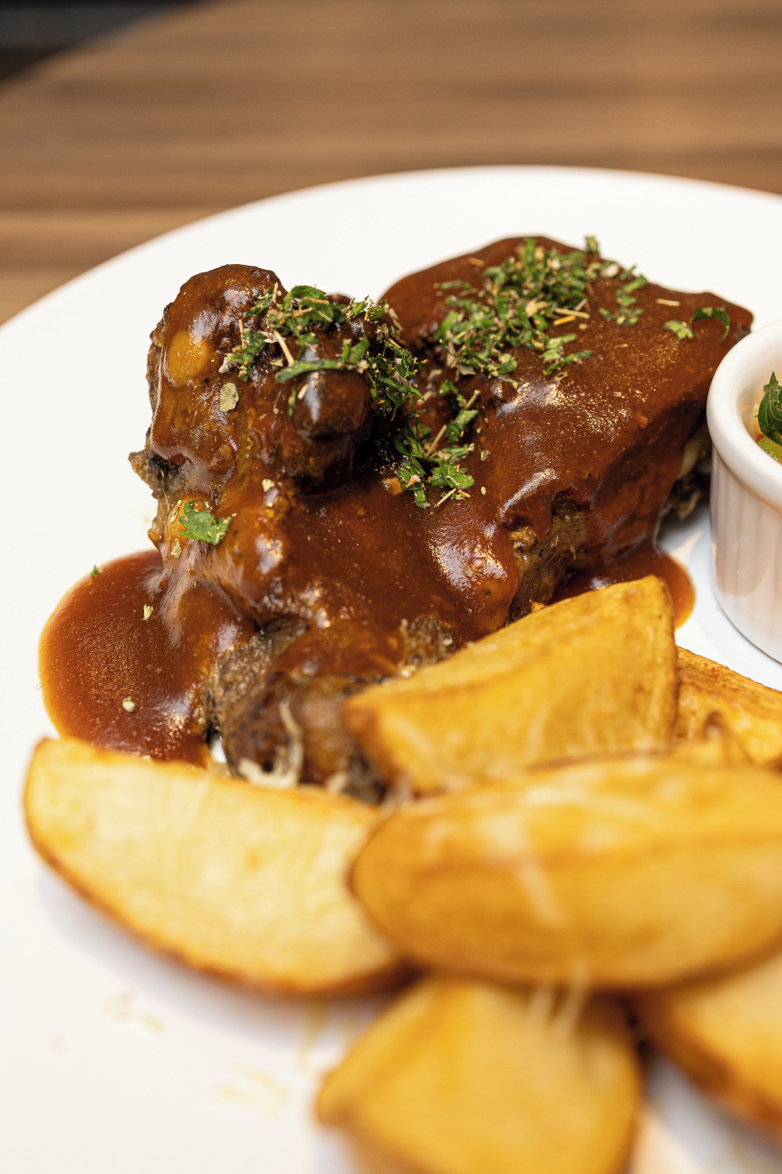 A plate of meat with gravy and potato wedges.