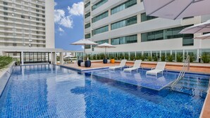 Una piscina en la azotea con sillones de descanso y sombrillas, rodeada de edificios modernos.