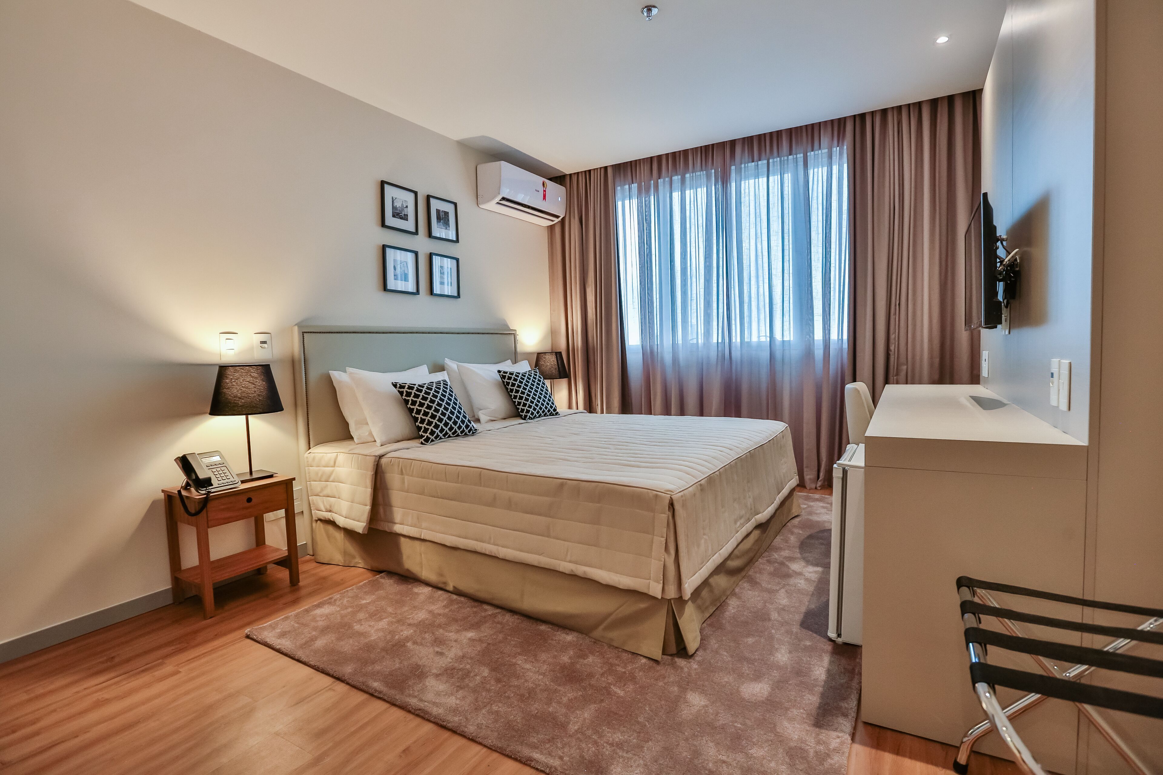 A modern hotel room with a bed, bedside table with a lamp, a desk, and a TV mounted on the wall.