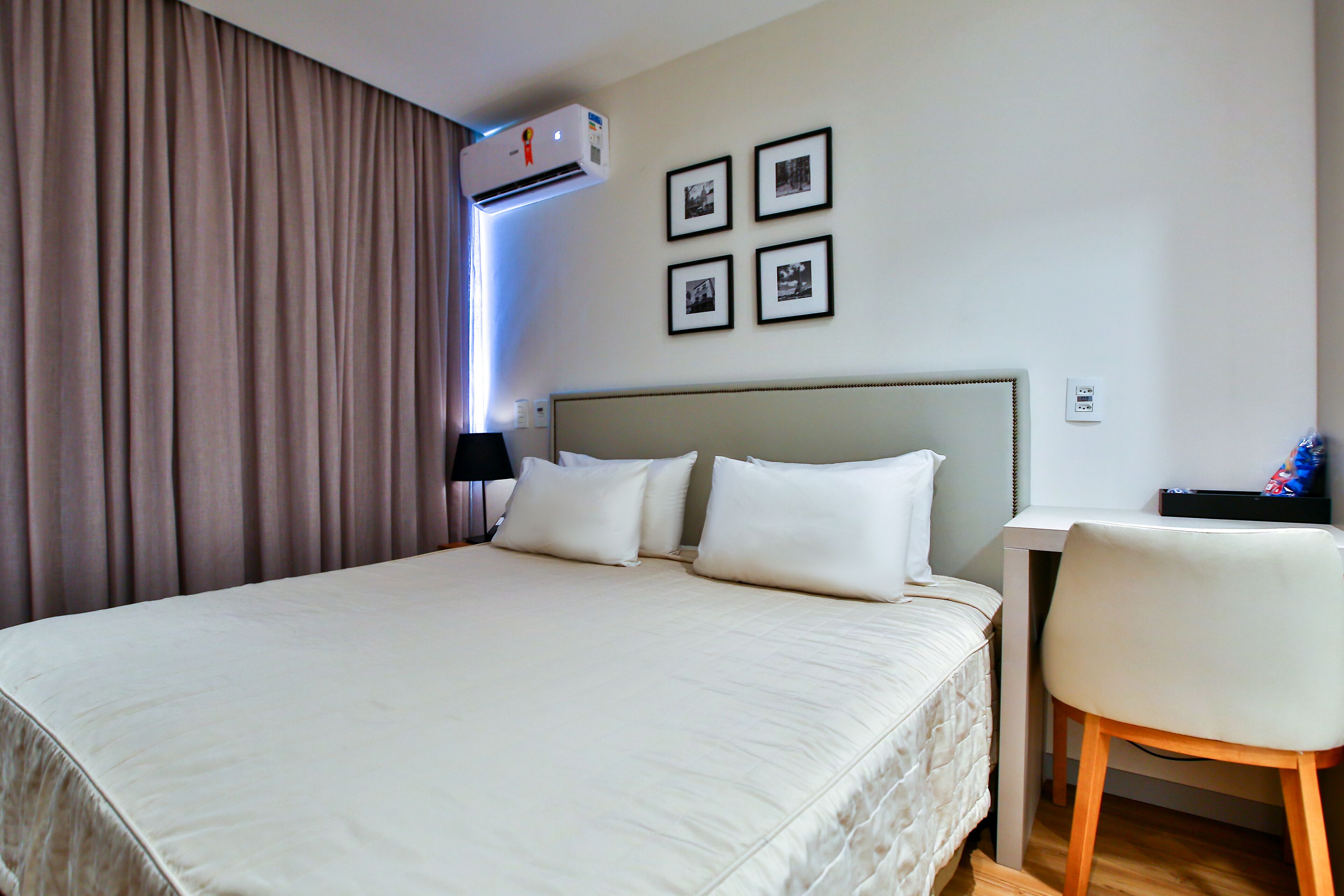 A hotel room with a large bed, a desk, a chair, and a wall-mounted air conditioner.