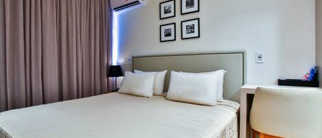 A hotel room with a large bed, a desk, a chair, and a wall-mounted air conditioner.
