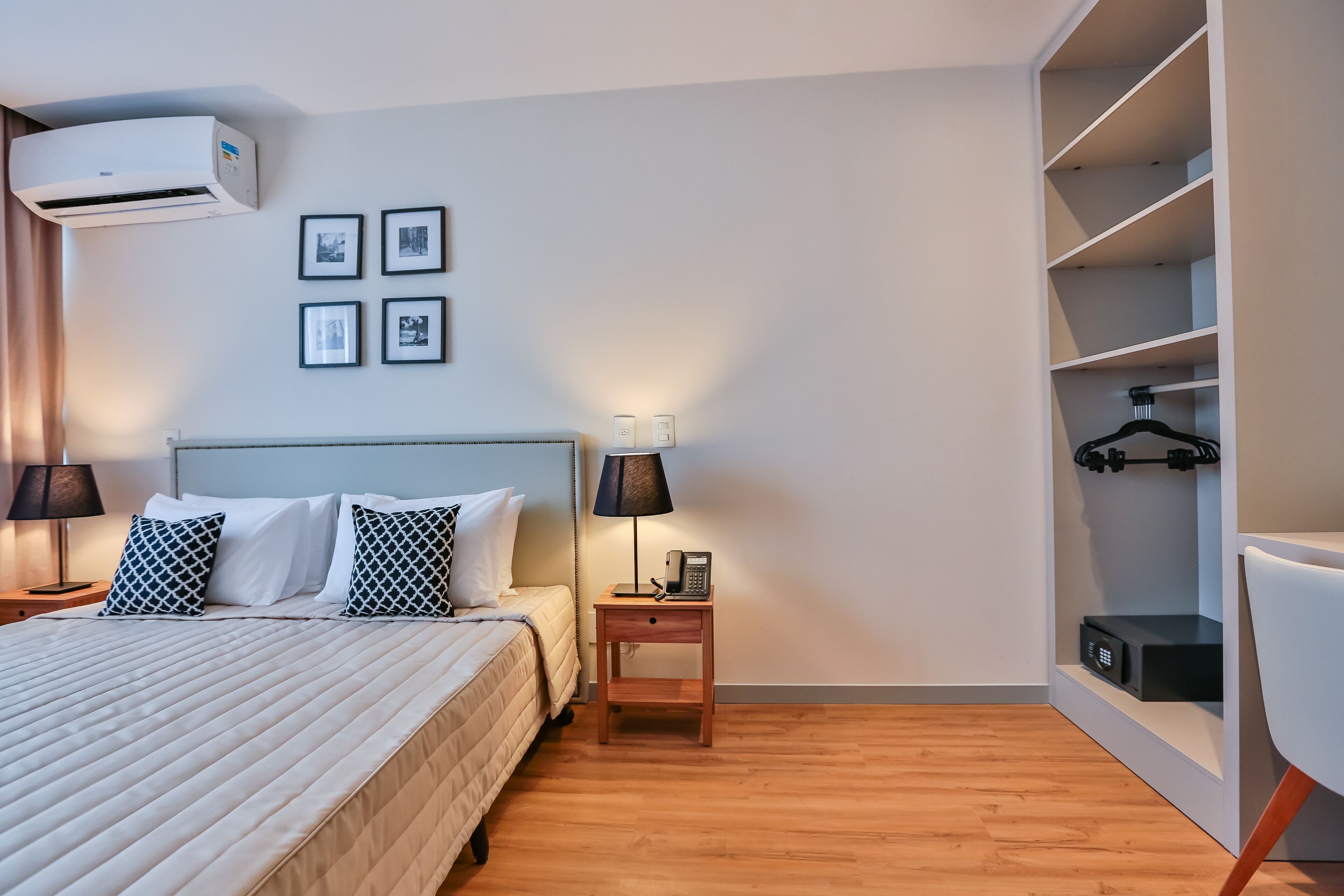 A neatly arranged hotel room with a bed, bedside tables, a lamp, an air conditioner, and a wardrobe.