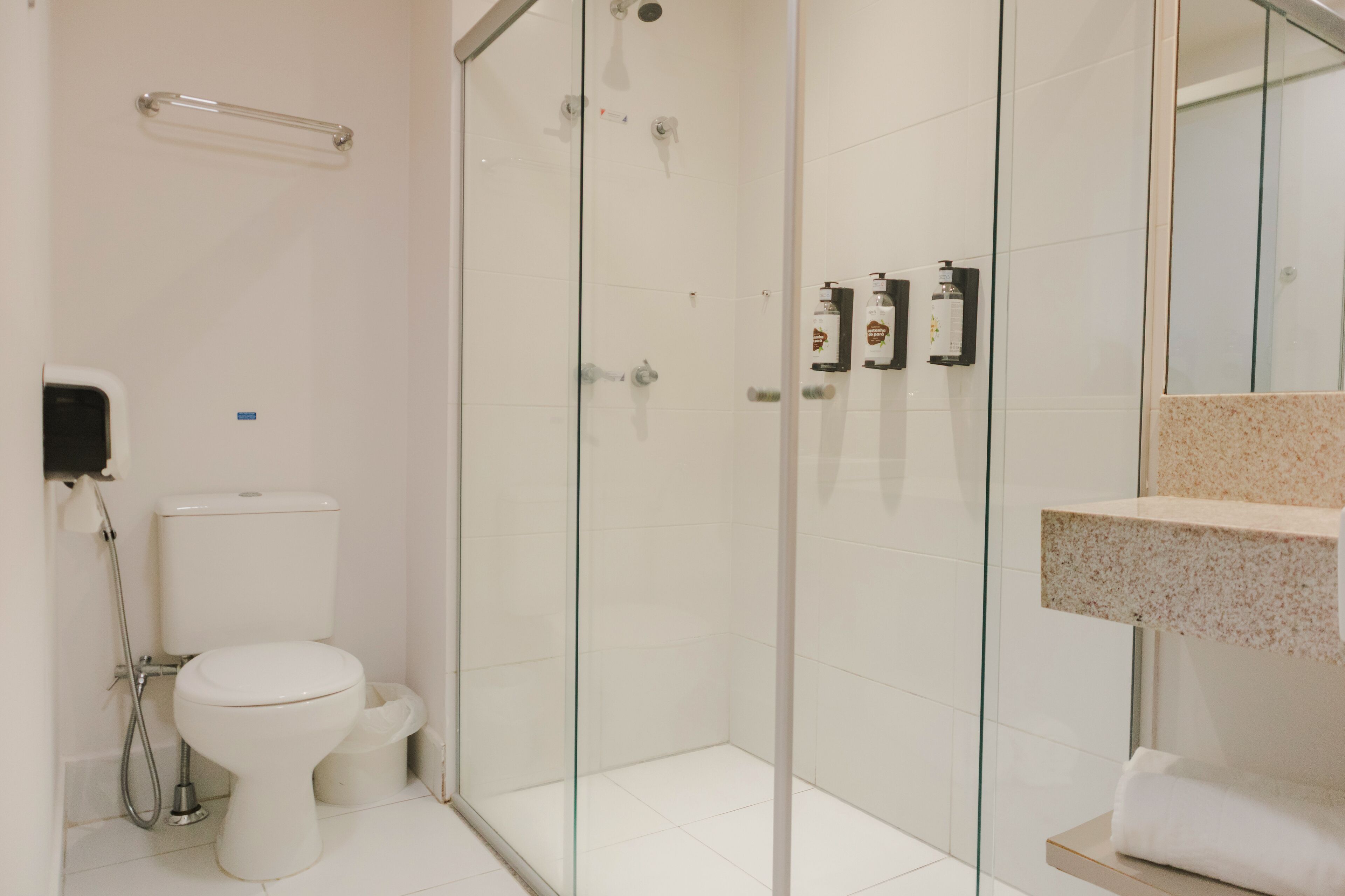 A modern bathroom with a glass-enclosed shower, a toilet, and a sink with a marble countertop.