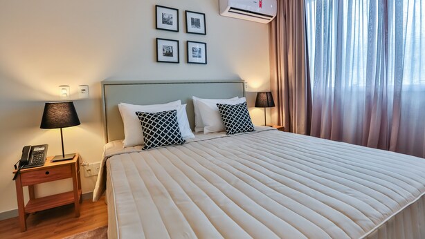 Habitación de hotel con una cama grande, dos mesitas de noche con lámparas, un equipo de aire acondicionado y una ventana con cortinas.