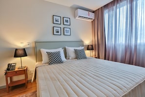 Ein Hotelzimmer mit einem großen Bett, zwei Nachttischen mit Lampen, einer Klimaanlage und einem Fenster mit Vorhängen.