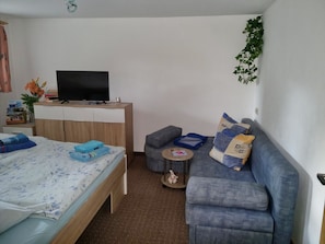A room with a bed, a sofa, a small table, a television, and a plant. - Apartment - FW SPRC 0141 (Parchtitz)