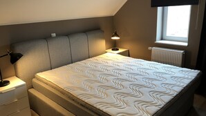 Une chambre à coucher avec un lit, une table de chevet, une lampe, une fenêtre et un radiateur.