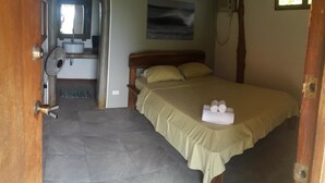 Een slaapkamer met een bed, een ventilator, een wastafel en een raam.