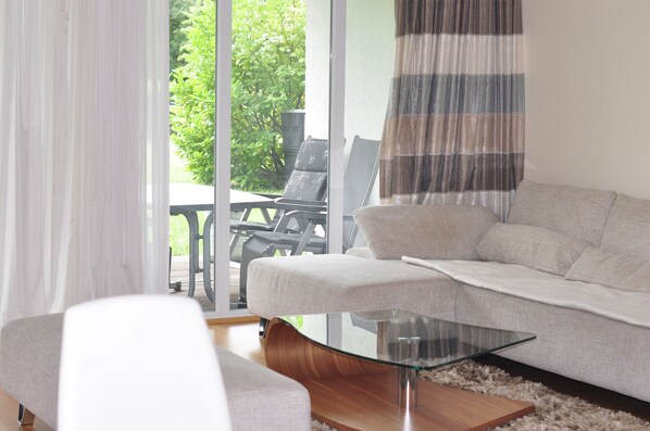 A modern living room with a sofa, a glass coffee table, and a view of an outdoor patio area.