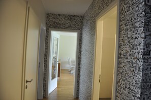 A hallway with patterned wallpaper, a door leading to a bedroom, and a wooden floor.